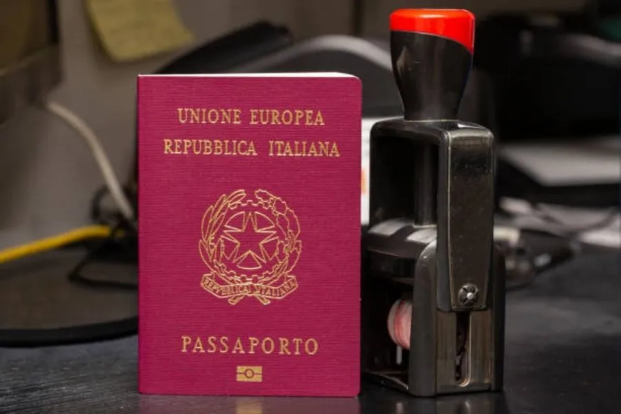 Imagem mostra passaporte italiano com carimbo ao lado.